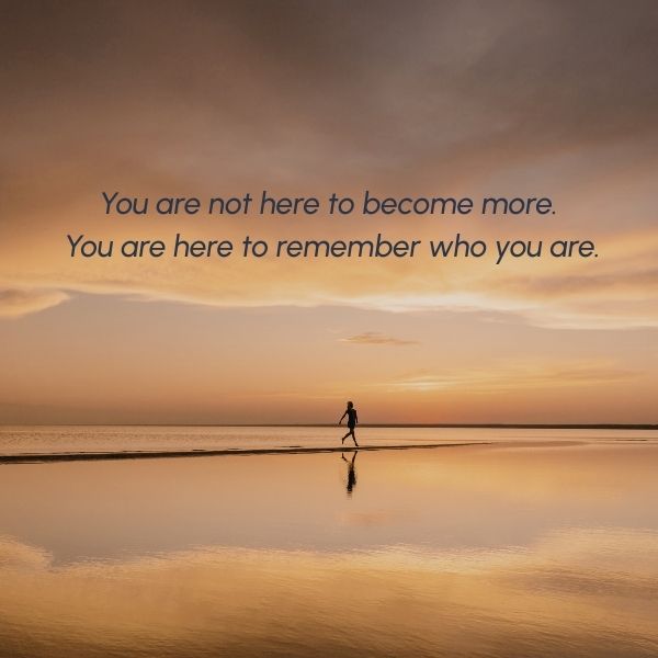 A woman walking along a calm shoreline at sunset with the words “You are not here to become more. You are here to remember who you are.”